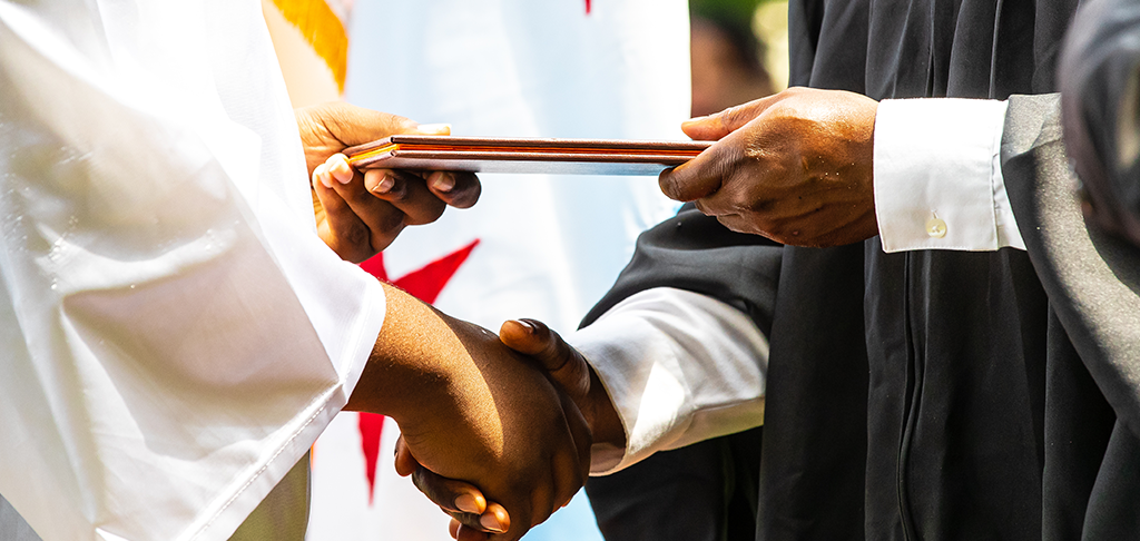 Closeup of the hands of a CPS official shaking hands with a graduate and passing off a diploma