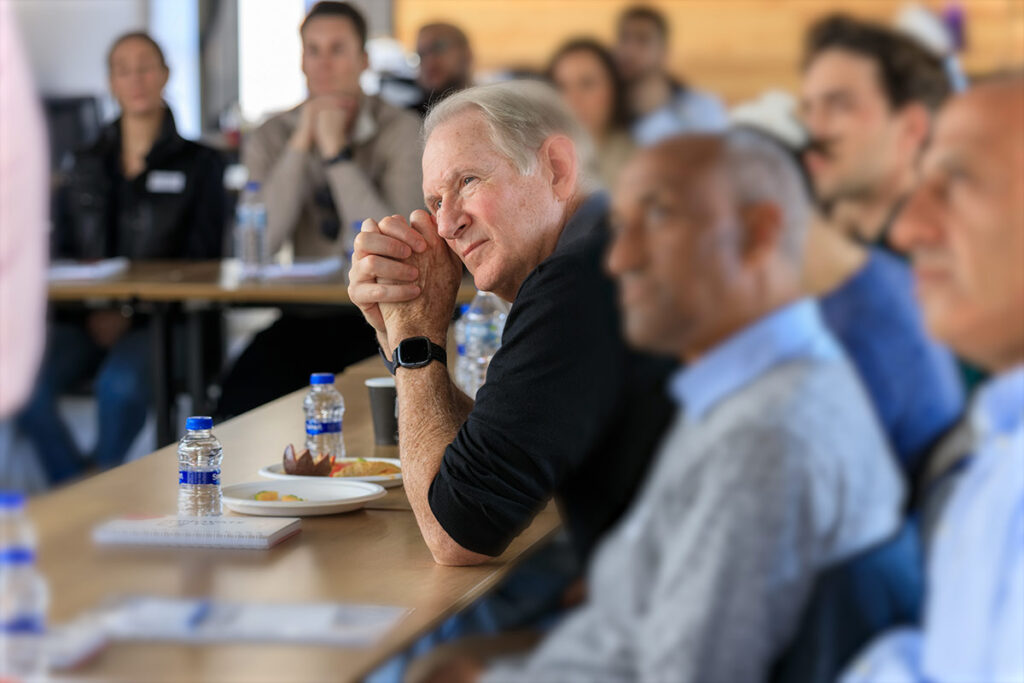 Jim Crown leans forward listening to a presentation from social impact partners